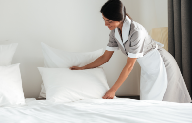 Femme de chambre disposant un oreiller sur un lit fraîchement préparé dans une chambre lumineuse.