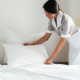 Femme de chambre disposant un oreiller sur un lit fraîchement préparé dans une chambre lumineuse.
