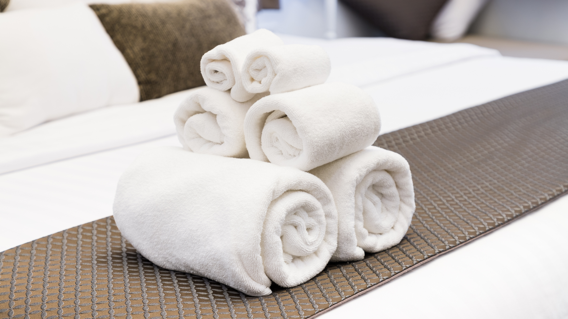Serviettes de bain blanches roulées et disposées sur un lit au linge soigné.